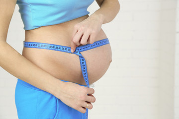 Young pregnant woman with measuring tape on light background