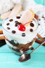 Tasty tiramisu dessert in glass, on color wooden background
