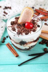 Tasty tiramisu dessert in glass, on color wooden background