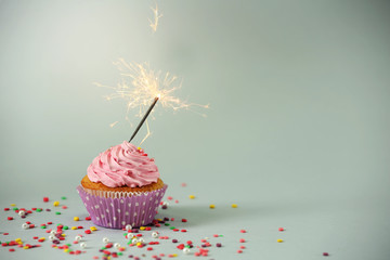 Cupcake with sparkler on grey background