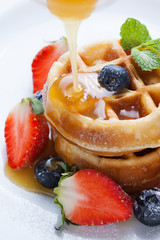 pouring caramel sauce on waffles with strawberry and blueberry