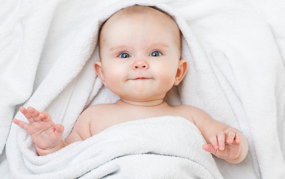 Cute funny smiling baby lying on back in bathing towel