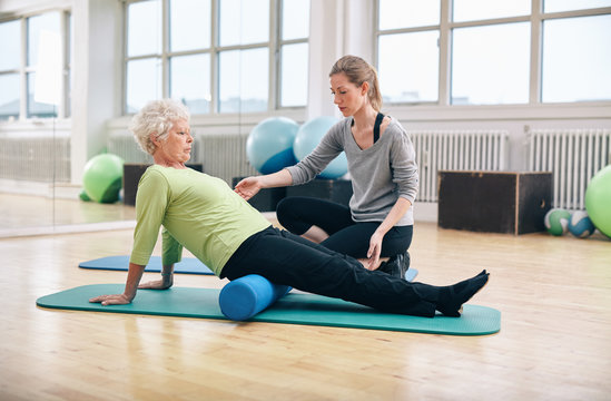Old woman using foam roller with personal trainer