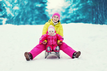 Fototapeta na wymiar Mom with a child sledding and having fun in winter day
