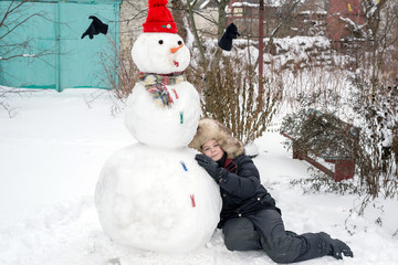 The boy in a fur hat around snowman