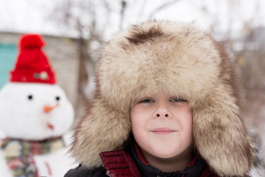 The boy in a fur hat around snowman