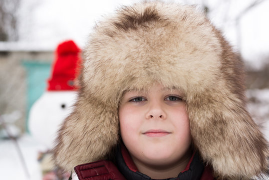 The boy in a fur hat around snowman