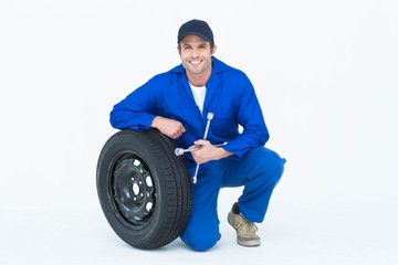 Fototapeta na wymiar Mechanic leaning on tire while holding wheel wrenches