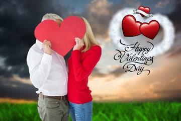 Composite image of couple embracing and holding heart over faces