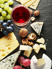 Different types of cheeses with wine glass and fruits.