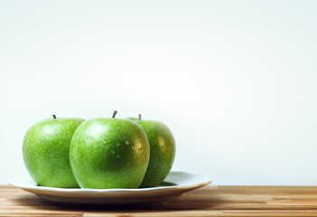 green apples in plate on wooden table