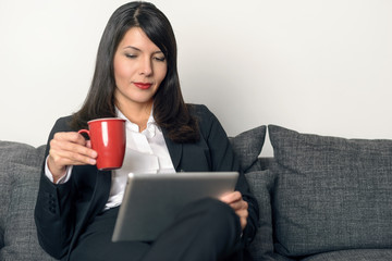 Attraktive Geschäftsfrau trinkt Kaffee und liest auf Tablet