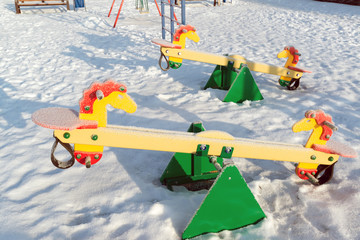 snow covered swing and slide at playground in winter