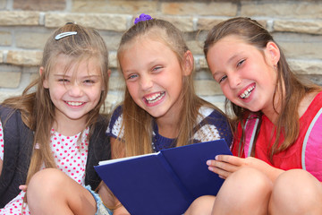 happy schoolgirls with a book outdoors