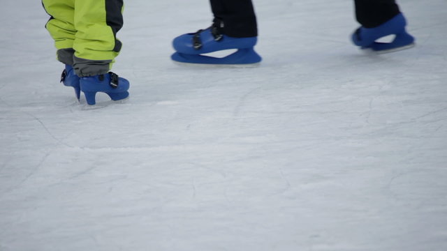 Legs of mother skating around it's child on skate rink