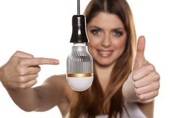 Young smiling woman pointing on LED bulb, and showing thumb up
