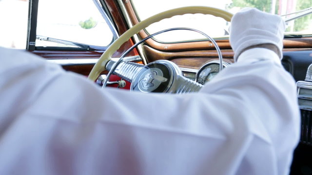 Man in white shirt steering a wheel in vintage car