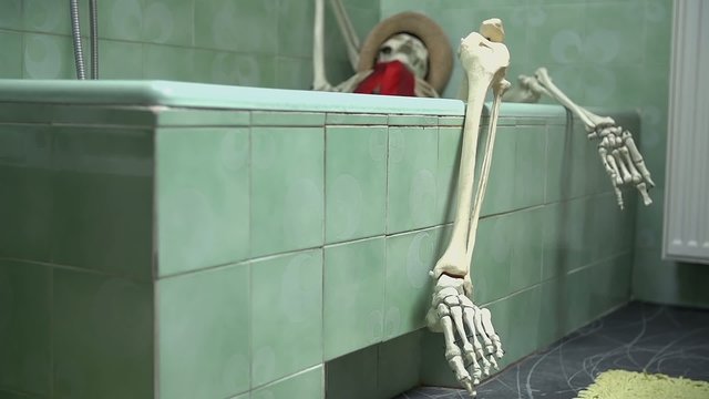 Skeleton enjoying a bath with his leg hanging out of the bathtub