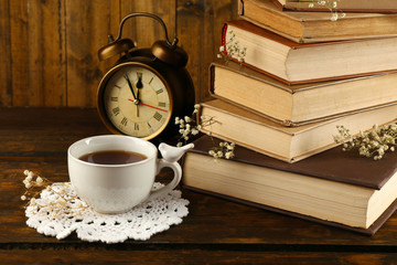 Cup of tea with books and clock on wooden background