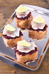 Rye toasts with herring and beets on tray on wooden background