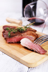 Steak with herbs on wooden stand and wine on table close up