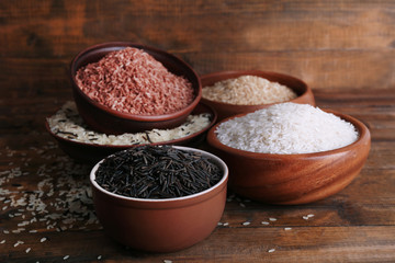 Different kinds of rice in bowls on wooden background