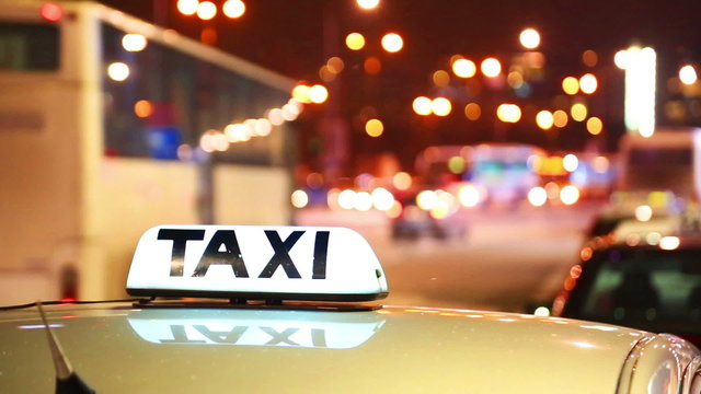Shining Taxi inscription against passing cars on night street