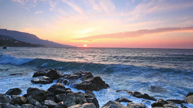 Waves break about stones at sunrise over the sea