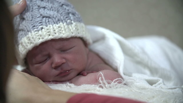 Baby with blue cap rests while being covered with white blanket