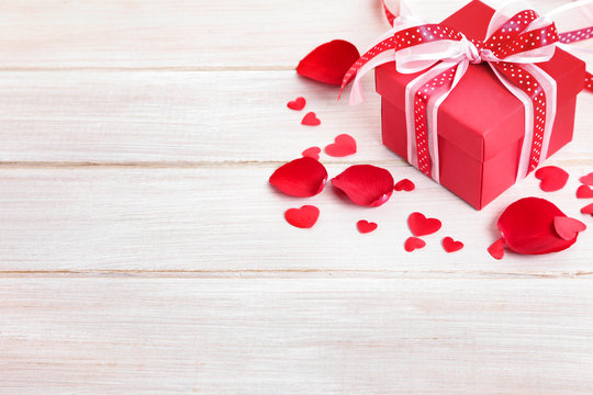 Valentine background of gift box and rose petals on white wood.