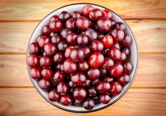 Juicy red grapes in bowl on wooden background