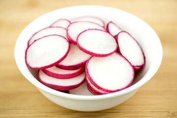 Sliced radishes in bowl on rustic wooden background