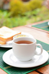 Hot tea in white cup with sliced bread on green mat