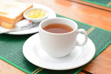 Hot tea in white cup with sliced bread on green mat