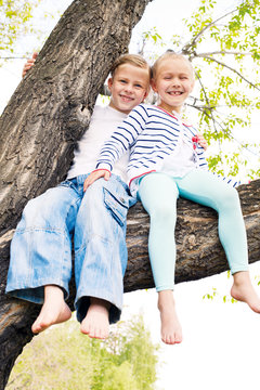 two blonde little girl sitting on a tree and waving her bare fee