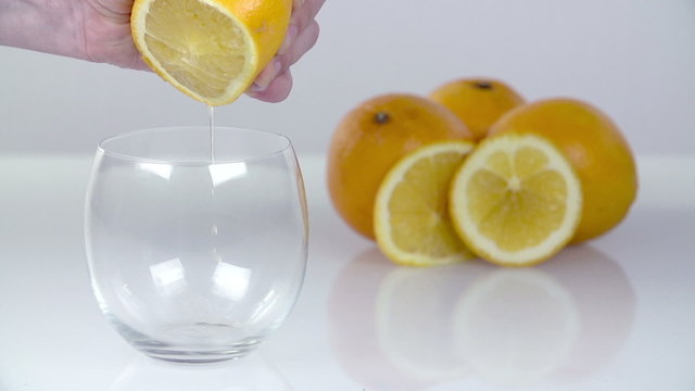 Squeezing a lemon juice into transparent glass on white background
