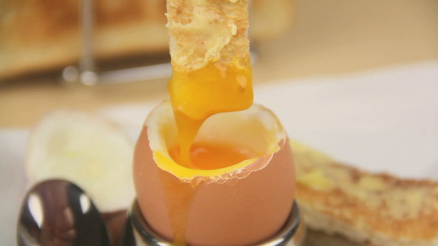 Dipping a piece of toast into the yolk of a boiled egg.