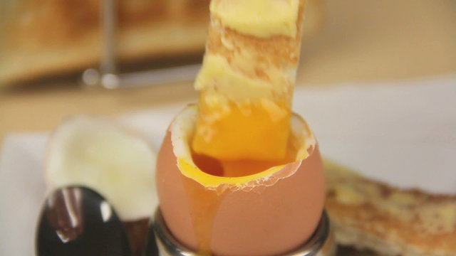 Dipping a piece of toast into the yolk of a boiled egg.