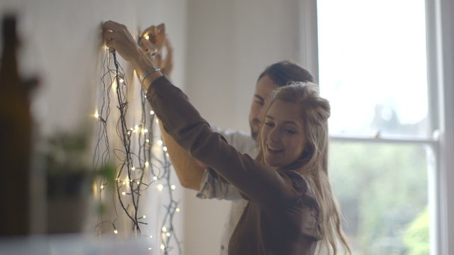 Young man and woman decorating wall with fairy lights