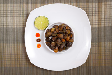 A plate with uncooked mussels and lime with sauces on a brown