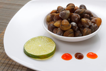 A plate with uncooked mussels and lime with sauces on a brown