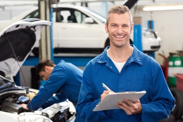 Smiling mechanic writing on clipboard