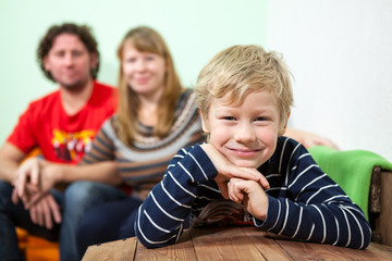 Cheerful young smiling son sits on foreground, parents on sofa