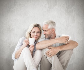 Composite image of happy couple sitting holding mugs