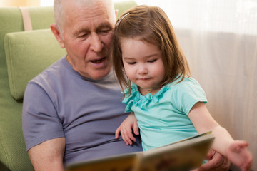 Cute little girl reading a book with her grandfather