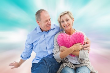 Composite image of happy mature couple with heart pillow