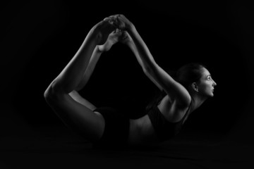 Young woman doing yoga stretches on black background