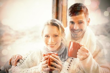 Loving couple in winter clothing with coffee cups against window