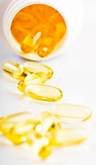 shiny yellow vitamin e fish oil capsule spilling out of pill bot