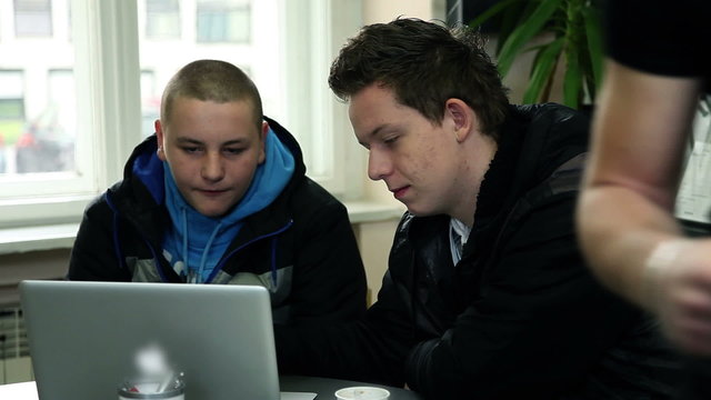 Two students in school cafeteria talking and looking at computer